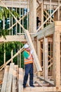 Carpenter holding large beam while builds wooden frame house near the forest. Royalty Free Stock Photo