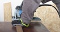 Carpenter cuts wood lath electric hand tool circular saw on desk, on background oriented strand board Royalty Free Stock Photo