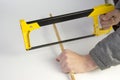 A carpenter cuts a wooden stick with a hand saw on a white background