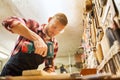 Carpenter with drill drilling plank at workshop