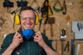 A carpenter in goggles and earmuffs removes a protective respirator.