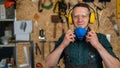 A carpenter in goggles and earmuffs removes a protective respirator.