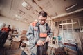 Carpenter handyman sharpening pencil with pocket knife on woodwork workshop table.