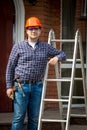 Carpenter in hard hat posing at metal step ladder