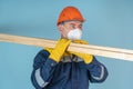 The carpenter holds wooden planks on his shoulders. A construction worker in a protective helmet, gloves and a respirator carries Royalty Free Stock Photo