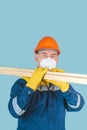 The carpenter holds wooden planks on his shoulders. A construction worker in a protective helmet, gloves and a respirator carries Royalty Free Stock Photo