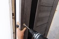 A carpenter is installing a doorknob with a latch on a wooden door. Close-up of a hand with a tool
