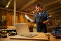 Carpenter looking at blueprints plans standing near laptop in the carpentry workshop