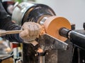 Carpenter man is shaving surface of the wooden bowl. Spinning wood wheel. Carving outside forming a round detail. Royalty Free Stock Photo