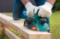 A carpenter planes a wooden board with an electric plane. Planing wooden plank with a electric plane. Close-up on hands with an Royalty Free Stock Photo