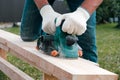 A carpenter planes a wooden board with an electric plane. Planing wooden plank with a electric plane. Close-up on hands with an Royalty Free Stock Photo