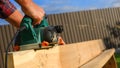 A carpenter planes a wooden board with an electric plane. Planing wooden plank with a electric plane. Close-up on hands with an Royalty Free Stock Photo