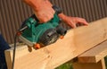 A carpenter planes a wooden board with an electric plane. Planing wooden plank with a electric plane. Close-up on hands with an Royalty Free Stock Photo