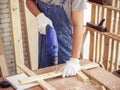 carpenter`s hands wearing gloves using electric drilling machine drilling wood plank