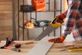Carpenter sawing wooden plank at table in workshop, closeup. Space for text Royalty Free Stock Photo