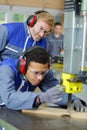 Carpenter training male apprentice to use mechanized saw