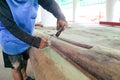 A carpenter using a chisel and axe to finishing the grooved surface of a large wood teak log inside of workshop Royalty Free Stock Photo