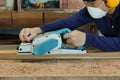 Carpenter using electric planer with wooden plank in carpentry workshop. He is wearing safety equipment Royalty Free Stock Photo