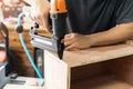 Carpenter using nail gun or brad nailer tool on wood box in a workshop ,furniture restoration woodworking concept. selective focus Royalty Free Stock Photo