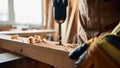 Carpenter wearing protective gloves and an apron, using a handheld power drill to create a hole in a piece of wood for a Royalty Free Stock Photo