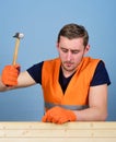 Carpenter, woodworker on calm face hammering nail into wooden board. Man, handyman in working uniform and protective