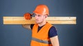 Carpenter, woodworker, strong builder on serious face carries wooden beam on shoulder. Man in helmet, hard hat and