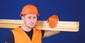 Carpenter, woodworker, strong builder on thoughtful face carries wooden beam on shoulder. Man in helmet, hard hat and