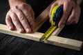 Carpenter or woodworker uses a construction tape to measure the length of a piece of wood. Hands of the master close-up at work.