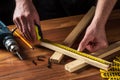 Carpenter or woodworker uses a construction tape to measure the length of a piece of wood. Hands of the master close-up at work.