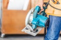 Carpenter working in wood workshop. Handyman manual worker in tools belt and holding circular saw in his hands Royalty Free Stock Photo