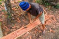 Carpenter works with hand tool a tree trunk. Worker on island of Bali sculpts a trough in a wooden beam. Heavy manual job