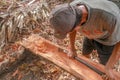 Carpenter works with hand tool a tree trunk. Worker on island of Bali sculpts a trough in a wooden beam. Heavy manual job