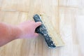 Carpet fitter master or floor person holding a spatula with wooden glue that is on the laid parquet. Photo scene from carpenter wo