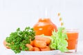 Carrot juice in beautiful glasses, cut orange vegetables and green parsley on white wooden background. Fresh orange drink. Close u