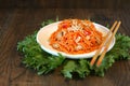 Carrot Korean chiken meat salad in a plate with chopsticks on wooden oak table and green salad leafs, fresh yellow pepper. Spicy