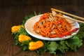 Carrot Korean chiken meat salad in a plate with chopsticks on wooden oak table and green salad leafs, fresh yellow pepper. Spicy