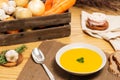 Carrot and potato soup on a wood table with vegetables in a crate alongside bread, silver spoon, pork belly, garlic and rosemary Royalty Free Stock Photo