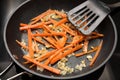 Carrot strips or julienne with onions and thyme are sauteed in a black frying pan, preparing vegetables for cooking a healthy