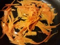 Carrot strips in oil cooking in frying pan