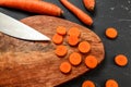 Carrots on wooden chopping and black working board, some of them cut to circles with chef knife, view from above