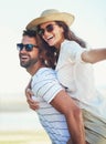 Carrying her to the ends of the earth. a handsome young man giving his girlfriend a piggyback ride at the beach. Royalty Free Stock Photo