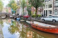 Cars and bicycles parked along street reflected with buildings over moored boats in canal.