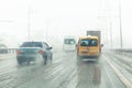 Cars drive along road with slush, snowstorm. City traffic in snow blizzard