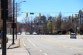 Cars driving along a wide street surrounded by buildings and bare winter trees with traffic signals and clear blue sky in midtown