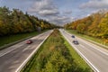 Cars are driving fast over a highway at the fall time, framed by beautiful trees, centred view. Royalty Free Stock Photo