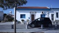 Cars are driving in front of the old white house with blue windows in Cyprus