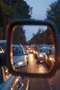 Cars with headlights queue in rearview mirror during evening traffic jam at dusk