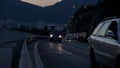 Cars with lights turned on on a four-lane road, divided by red lights, in the mountains in the evening