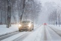 Cars moving on slippery snowy road at city street during heavy snowfall at evening in winter . Traffic obstacle due blizzard and