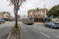 cars, trucks and buses driving along a street with lush green trees and autumn colored trees, apartments and retail stores